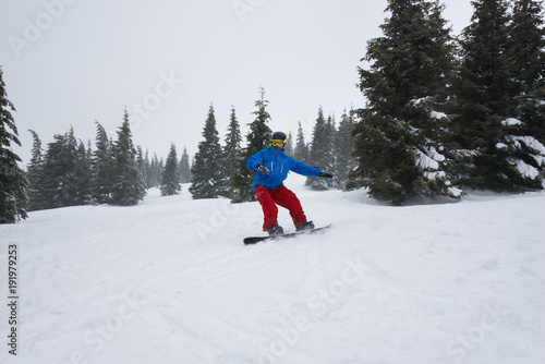 Snowboarder, wearing blue jacket, rides down a mountain slope