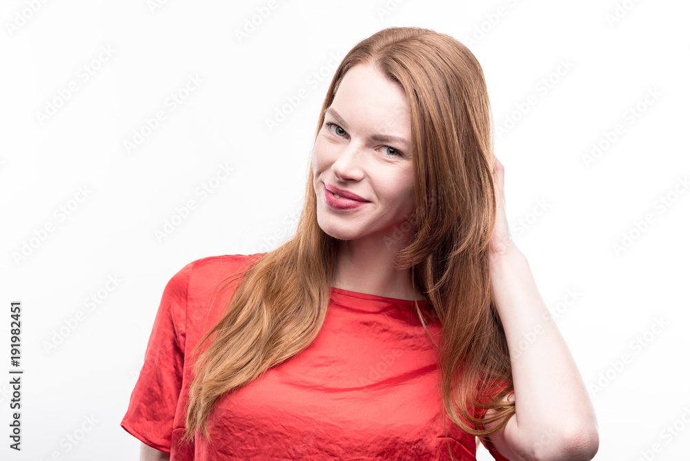 Appealing pose. The portrait of a gorgeous ginger-haired young woman in a red t-shirt posing with her hand in hair while standing isolated on a white background Appealing pose. The portrait of a gorgeous ginger-haired young woman in a red t-shirt posing with her hand in hair while standing isolated on a white background