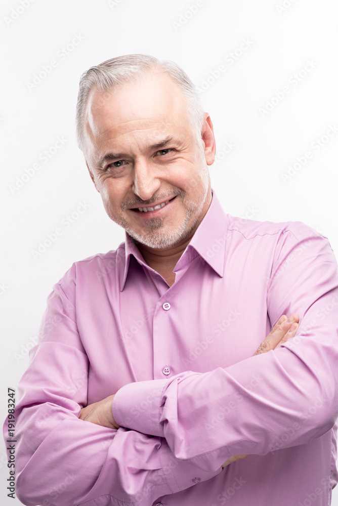 Powerful masculinity. Grey-haired senior man in a lilac shirt folding his arms across his chest and smiling at the camera while posing isolated on a white background Powerful masculinity. Grey-haired senior man in a lilac shirt folding his arms across his chest and smiling at the camera while posing isolated on a white background