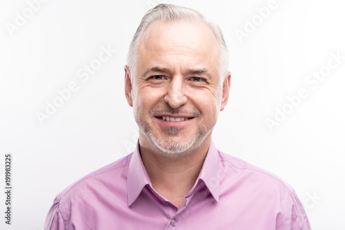 Refined maturity. The portrait of a handsome grey-haired bristled man in a lilac shirt smiling at the camera while posing isolated on a white background