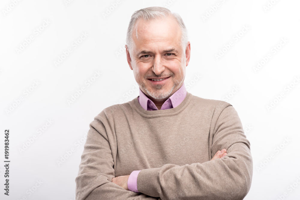 Power pose. Pleasant grey-haired bristled man folding his hands across his chest and smiling at the camera while posing isolated on a white background Power pose. Pleasant grey-haired bristled man folding his hands across his chest and smiling at the camera while posing isolated on a white background