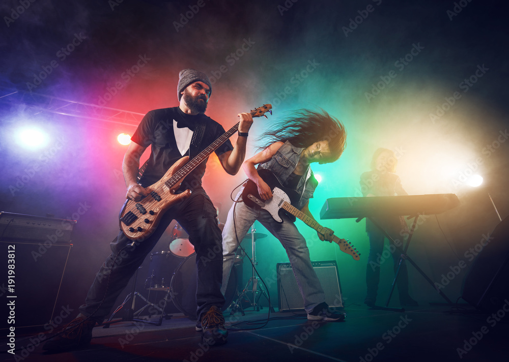 Rock band performs on stage. Guitarist, bass guitar and drums.