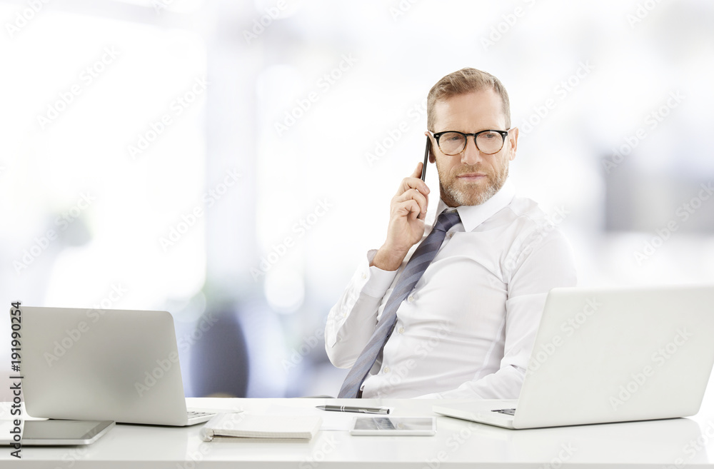 Businessman consulting on mobile phone with his client. Portrait of happy financial assistant business man using cell phone and making call while working on laptop at the office. Businessman consulting on mobile phone with his client. Portrait of happy financial assistant business man using cell phone and making call while working on laptop at the office.