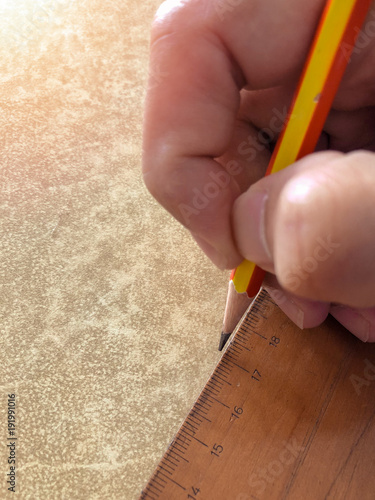 Close-up hand holding a pencil and a wooden ruler on the table. Warm glow effect.