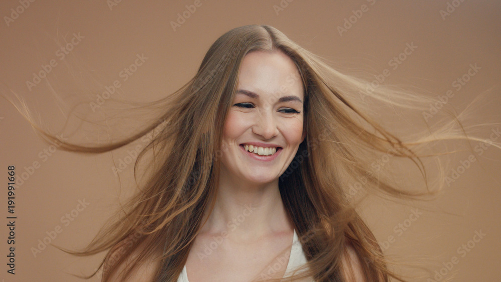 Fototapeta premium beauty woman model in studio on beige background with wind in hair bllowing it lauging a lot
