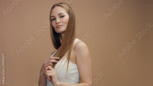 beauty woman model in studio on beige background touches her straight blonde hair and watching at camera