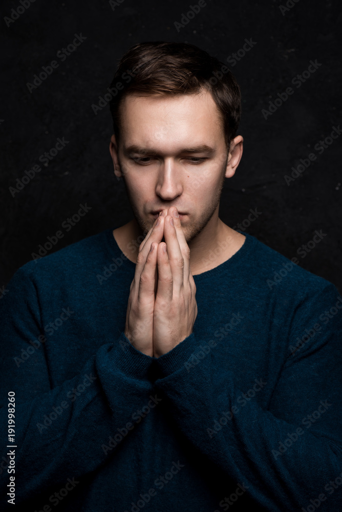 Handsome tough guy on a black background. Hands at the face. Praying. Cardigan. Portrait. Brawn. Force. Masculinity. Handsome tough guy on a black background. Hands at the face. Praying. Cardigan. Portrait. Brawn. Force. Masculinity.