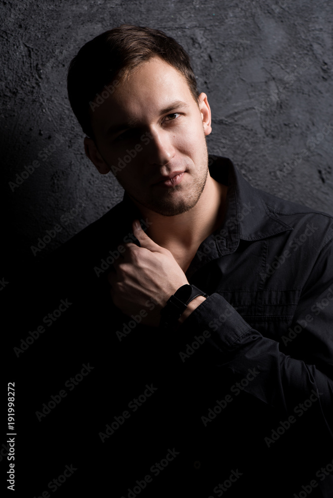 Fototapeta premium Portrait of a handsome muscular guy on a black background in a shirt. Adjusting the shirt. Black shirt. Force.