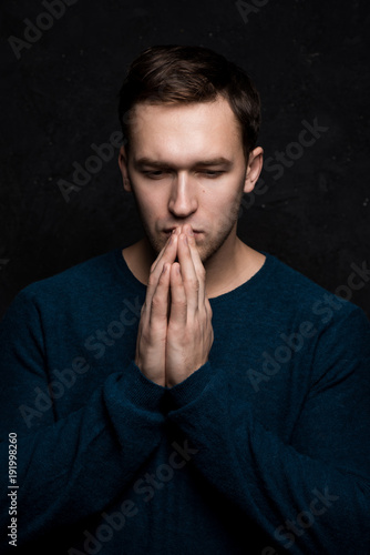 Handsome tough guy on a black background. Hands at the face. Praying. Cardigan. Portrait. Brawn. Force. Masculinity.
