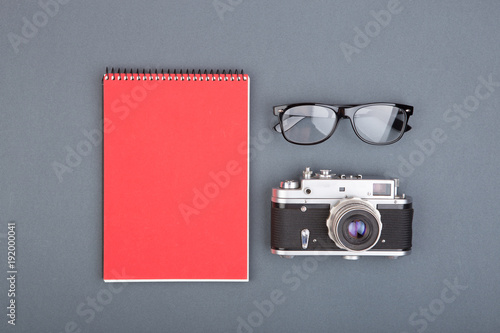 Journalist or blogger table - spiral blank notebook, pencil, camera and glasses on gray background, top view photo