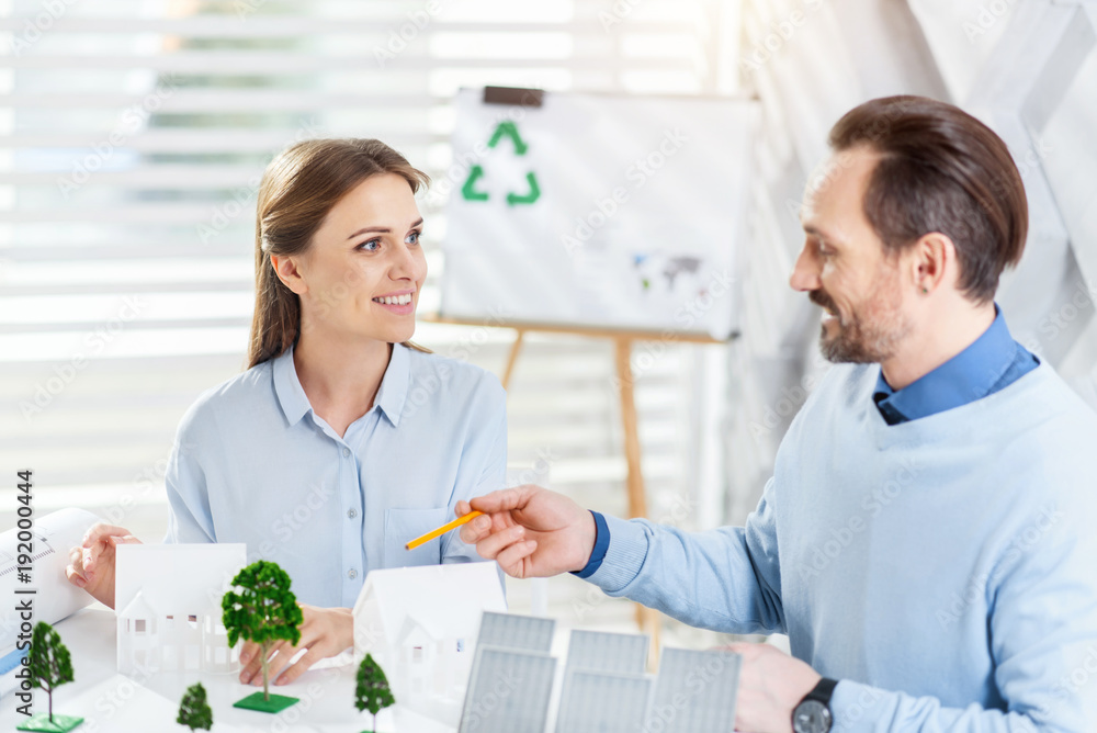 Recycling project. Attractive content bearded man smiling and working with his inspired colleague on an eco-friendly project while sitting at the table Recycling project. Attractive content bearded man smiling and working with his inspired colleague on an eco-friendly project while sitting at the table