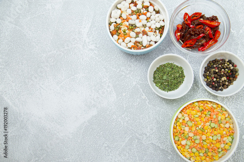 Set of raw ingredients for Italian cooking on stone table background. Black papper, sun dried tomatos, green dry species and beans. Set of healthy food products. Closeup