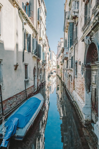 A small blue boat tied to a house with a brick wall in a narrow canal  Venice  Italy