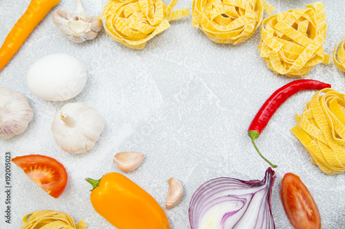 Set of raw ingredients for Italian cooking on stone table background. Red and yellow pappers, garlic, onion, pasta, eggs. Closeup and top view