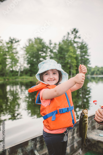 Father and daughter in boat on lake, daughter holding caught fish on line
