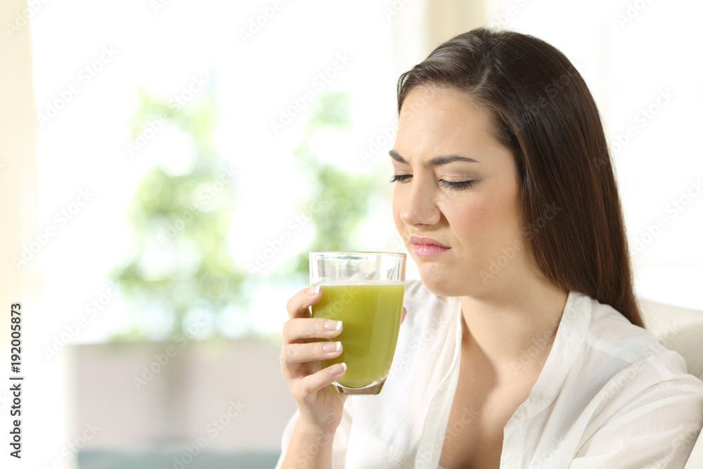 Disgusted woman tasting a vegetable juice with bad flavor Disgusted woman tasting a vegetable juice with bad flavor