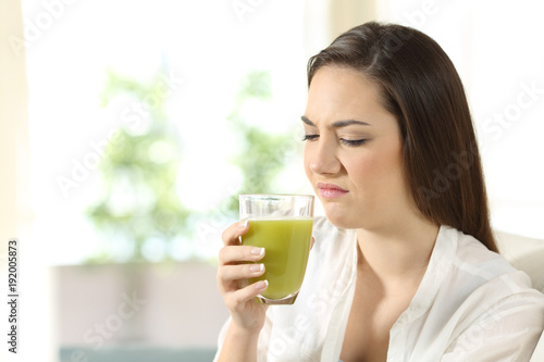Disgusted woman tasting a vegetable juice with bad flavor