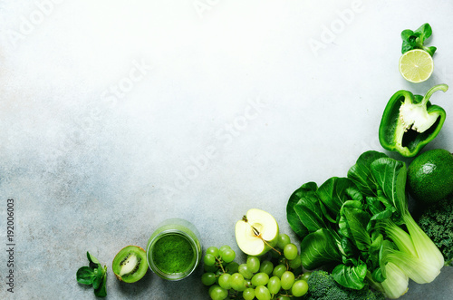 Green smoothie in glass jar with fresh organic green vegetables and fruits on grey background. Spring diet, healthy raw vegetarian, vegan concept, detox breakfast, alkaline clean eating. Copy space