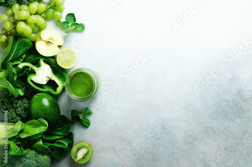 Green smoothie in glass jar with fresh organic green vegetables and fruits on grey background. Spring diet, healthy raw vegetarian, vegan concept, detox breakfast, alkaline clean eating. Copy space photo