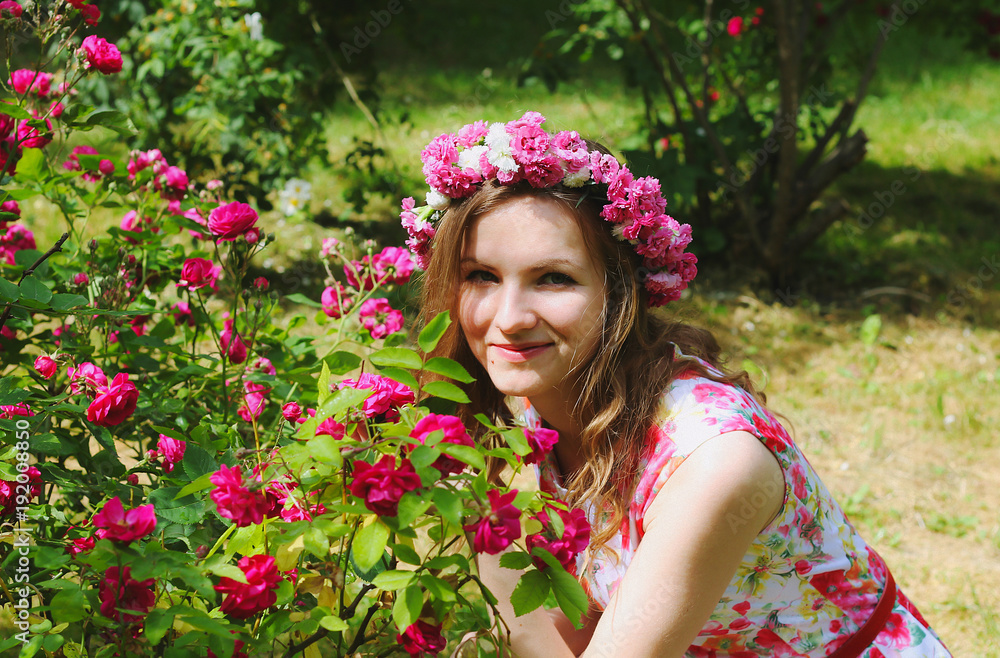 Beautiful girl in pink flower crown sits near the rose bush in green summer park. Pink floral dress. Spring woman photo. International women's day and mother's day holidays. Flower chaplet. Beautiful girl in pink flower crown sits near the rose bush in green summer park. Pink floral dress. Spring woman photo. International women's day and mother's day holidays. Flower chaplet.