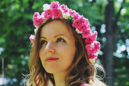Beautiful girl in pink flower crown looks into distance in summer park. Spring woman photo. International women's day and mother's day holidays. Flower chaplet. Pure sight. In profile portrait.