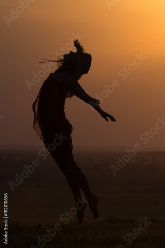 Silhouette of a beautiful young girl jumping in the sunset light