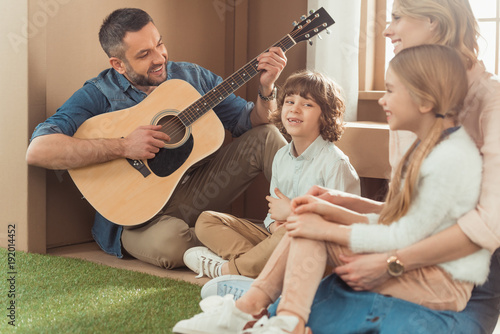 happy handsome father playing guitar for kids and wife at new cardboard house