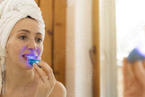 Woman is whitening teeth with special toothpaste and LED light at home. Beauty concept photo