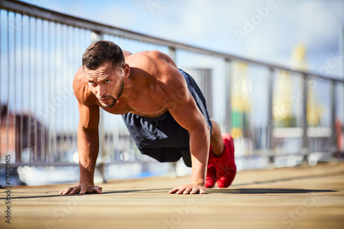 Determinated and athletic man doing pushups shirtless during workout in the city