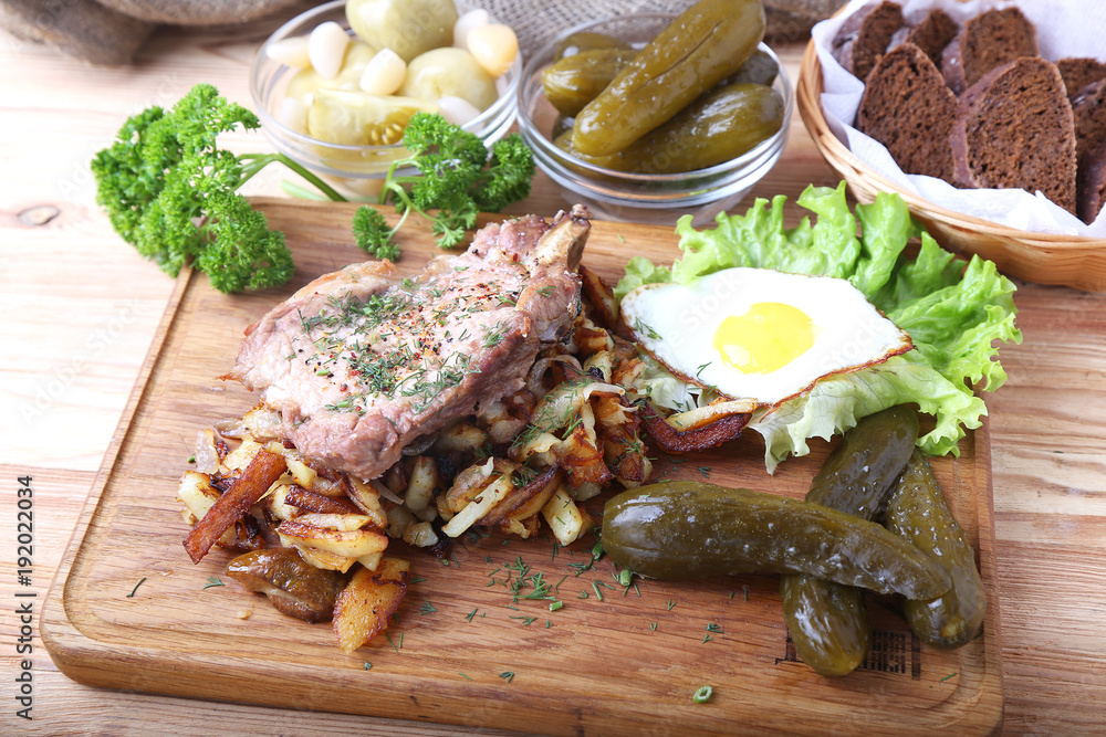Fried pork with potatoes, egg and pickle cucumber on a wooden board Fried pork with potatoes, egg and pickle cucumber on a wooden board