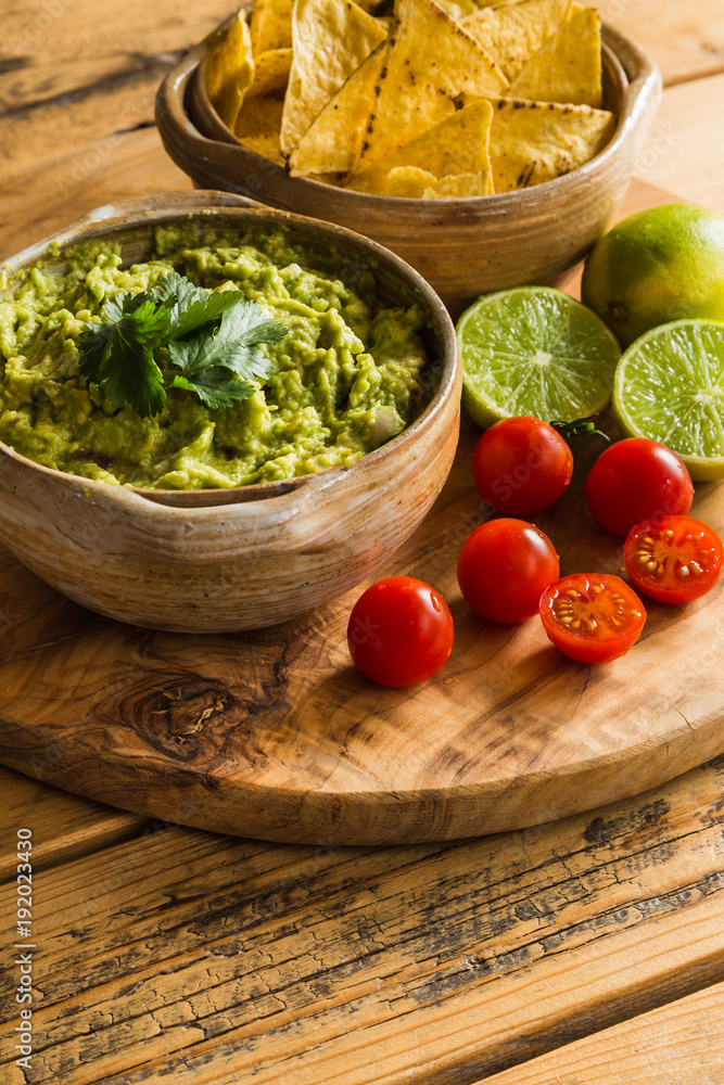 Bowl of guacamole dip with tortilla chips limes and cherry tomatoes Bowl of guacamole dip with tortilla chips limes and cherry tomatoes