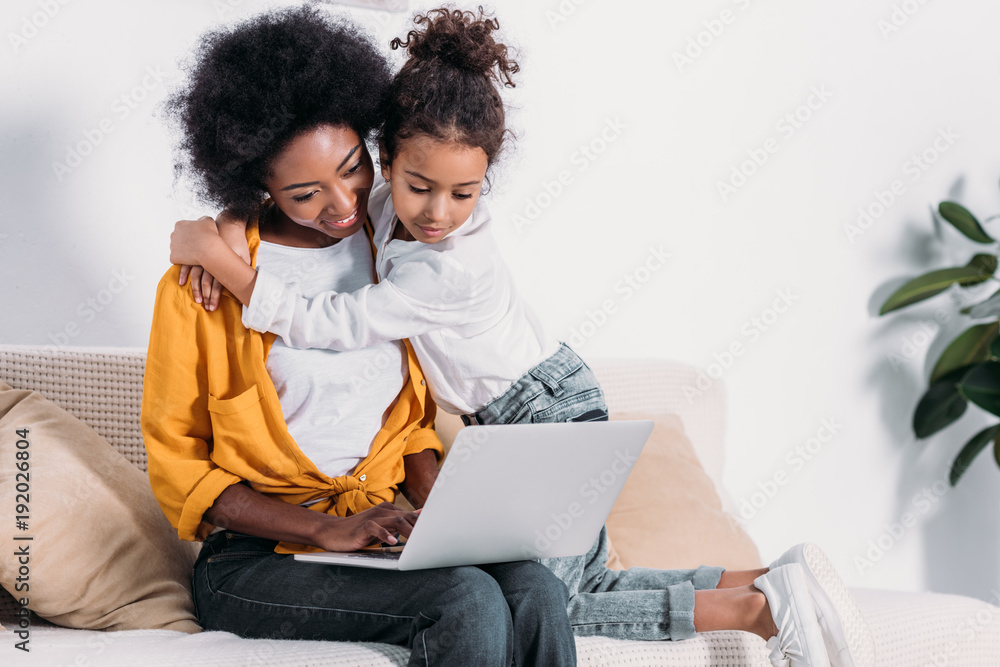 african american mother and daughter watching something on laptop at home