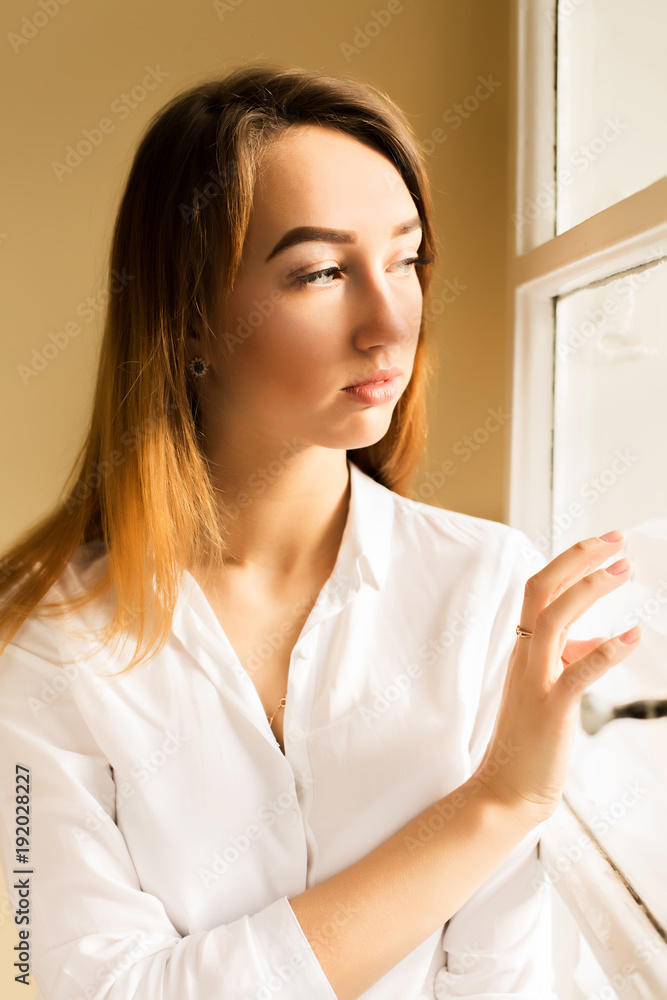 Closeup shot of elegant young woman in white shirt standing at the window Closeup shot of elegant young woman in white shirt standing at the window