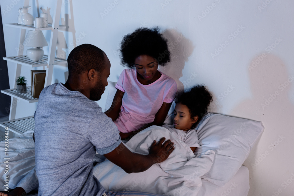 Obraz premium african american parents sitting near sleeping daughter at home