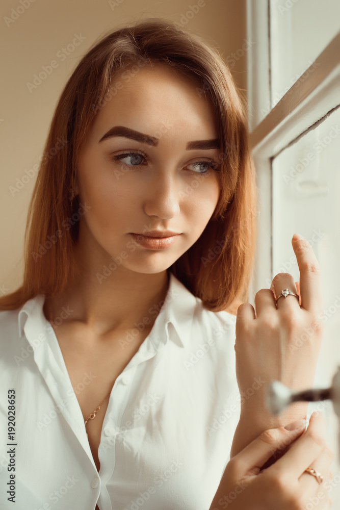Closeup shot of gorgeous brunette woman in white shirt standing at the window Closeup shot of gorgeous brunette woman in white shirt standing at the window