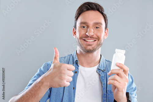 Handsome bearded man isolated on a white background with a bottle of pills. He trusts this medicine and he is happy because he wants to be healthy again.