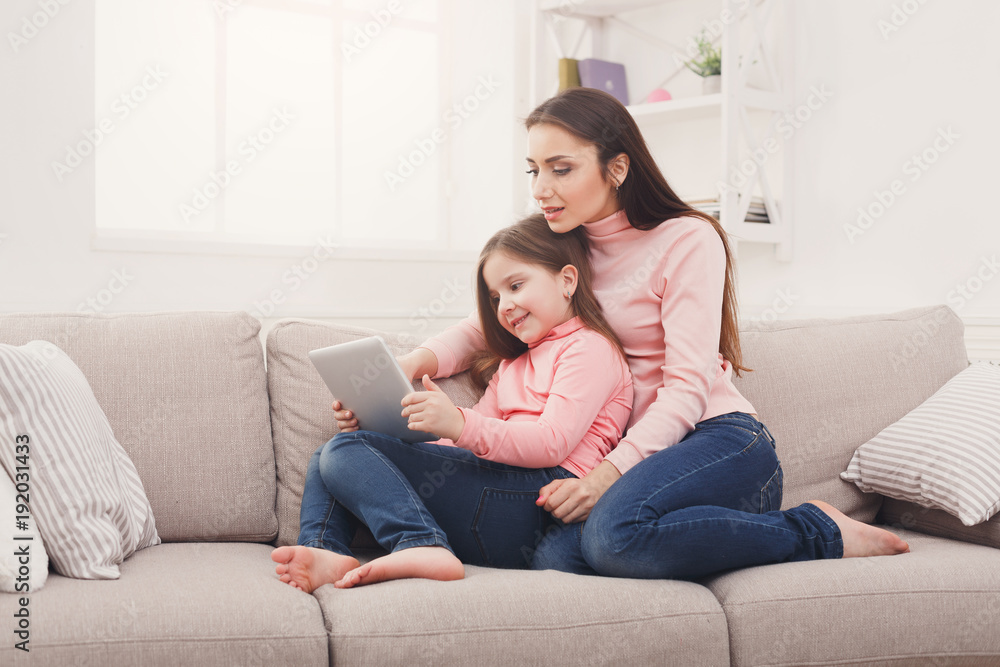 Little girl and her mom using a tablet at home