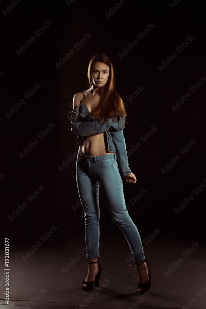 Fashionable young model in trendy jeans apparel posing in the dark