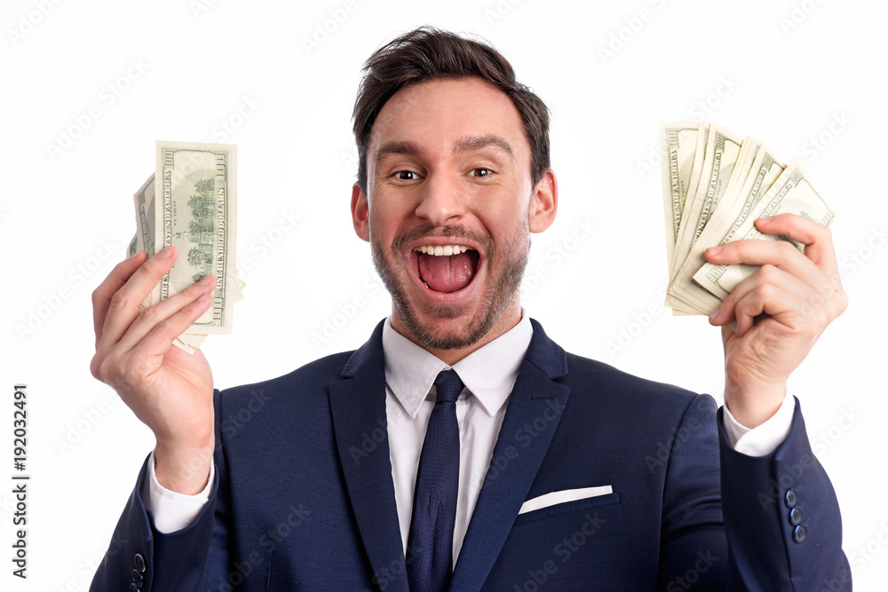 Handsome bearded young Businessman is holding a big stack of dollars and smiles isolated on a white background. Happy rich Guy in office suite with big money in his hands, he is a lucky winner Handsome bearded young Businessman is holding a big stack of dollars and smiles isolated on a white background. Happy rich Guy in office suite with big money in his hands, he is a lucky winner