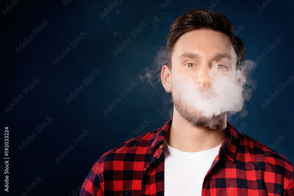 Handsome bearded man smoking electronic vape cigarette, Guy in a red t shirt smoking vapor, Man exhaled vapor on a dark studio background. Man smoking e-cigarette Handsome bearded man smoking electronic vape cigarette, Guy in a red t shirt smoking vapor, Man exhaled vapor on a dark studio background. Man smoking e-cigarette
