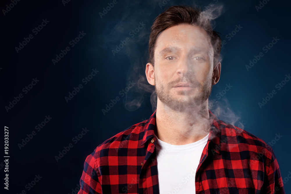 Handsome bearded man smoking electronic vape cigarette, Guy in a red t shirt smoking vapor, Man exhaled vapor on a dark studio background. Man smoking e-cigarette