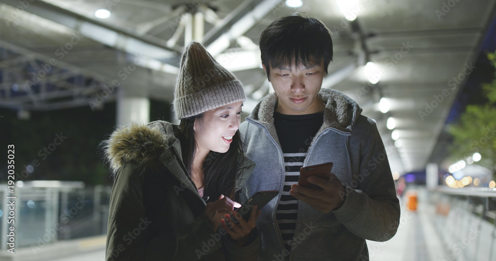 Couple using cellphone in city at night together