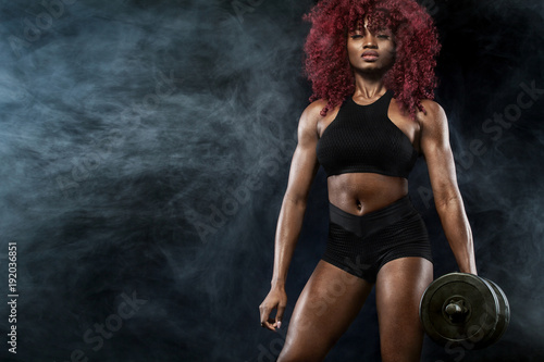 Sporty beautiful woman with dumbbells makes fitness exercising at black background to stay fit