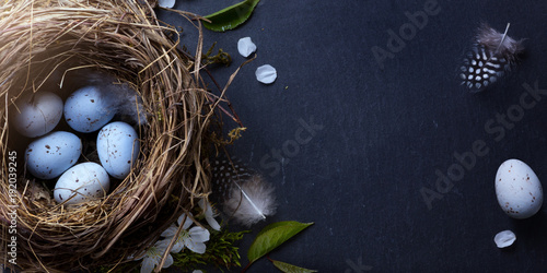 Happy Easter; Easter eggs in nest and spring flower on table background
