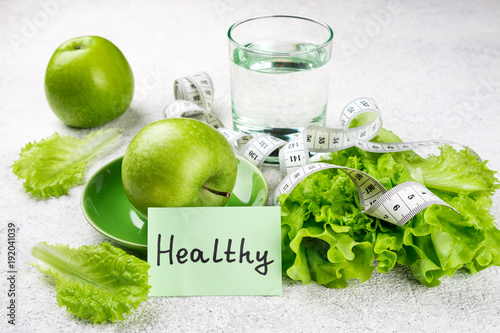 Healthy eating. Green apple, lettuce salad, glass of water, measuring tape. Dieting, slimming, weight loss and meal planning concept
