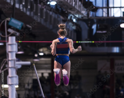 Foto Female pole vaulter clearing the bar