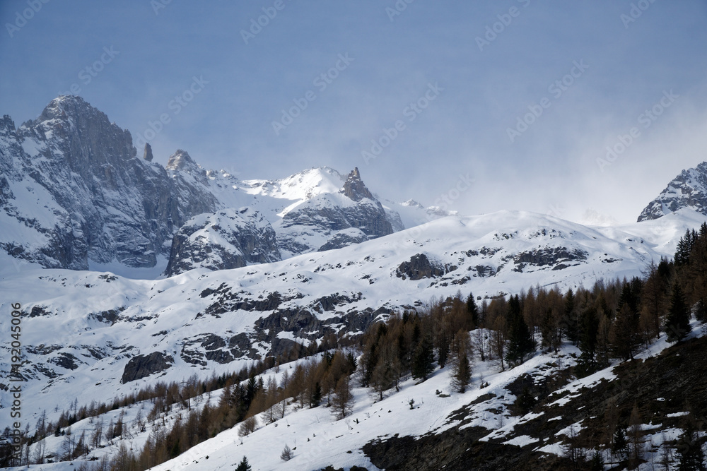 Mountains covered with snow, blue sky with clouds and winter forest near Mont Blanc Alpes, Italy