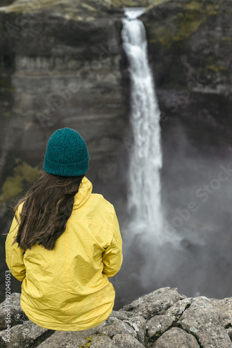 Caucasian woman sitting on cliff admiring waterfall photo