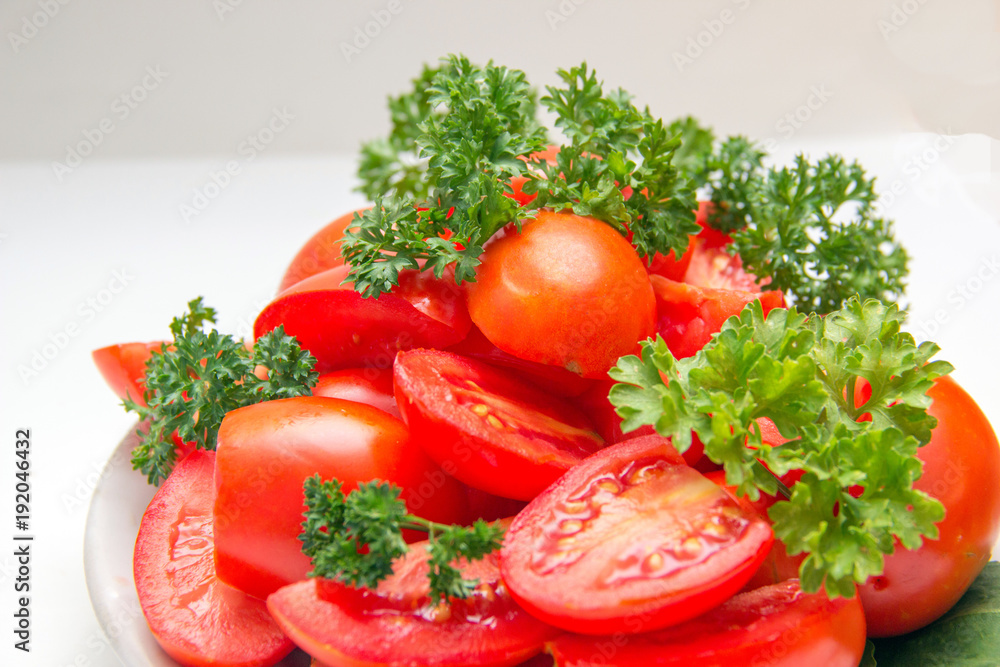 Slices of red ripe tomato and fresh herbs on a plate in the kitchen. Natural authentic still lifes, white back