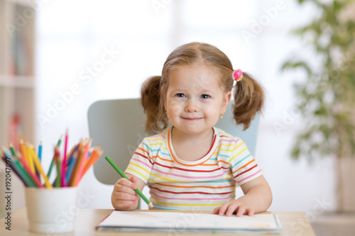 Cute happy little child girl drawing with pencils in daycare center